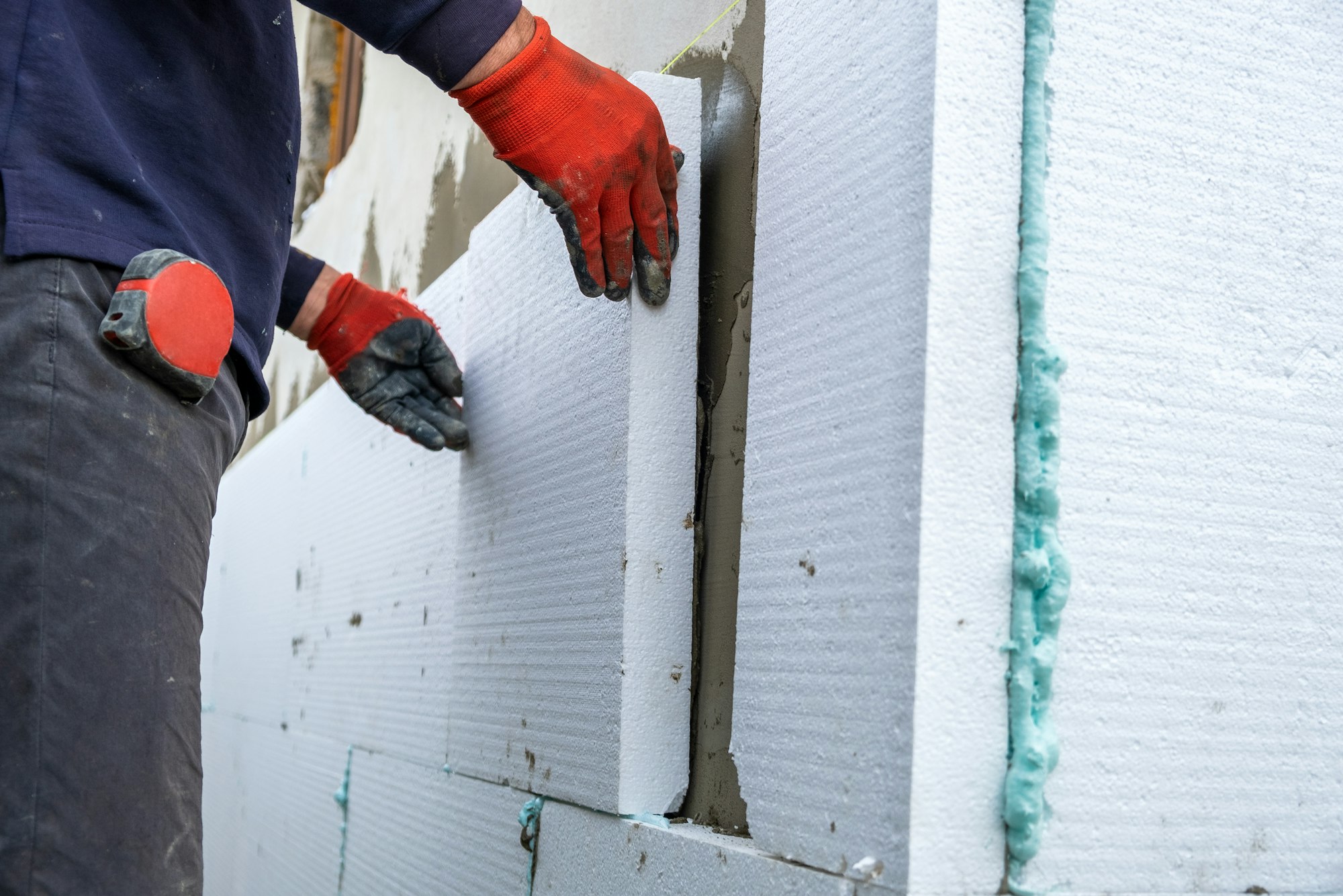 Construction worker installing styrofoam insulation sheets on house facade wall